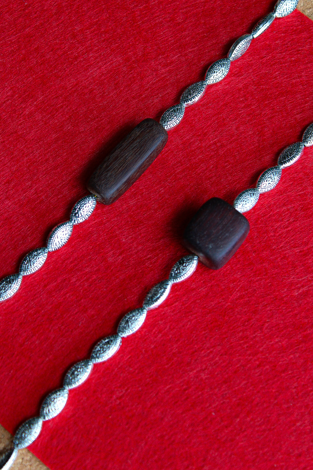 Two silver-toned twisted rope bracelets with dark brown wooden beads, laid diagonally on a textured red background.