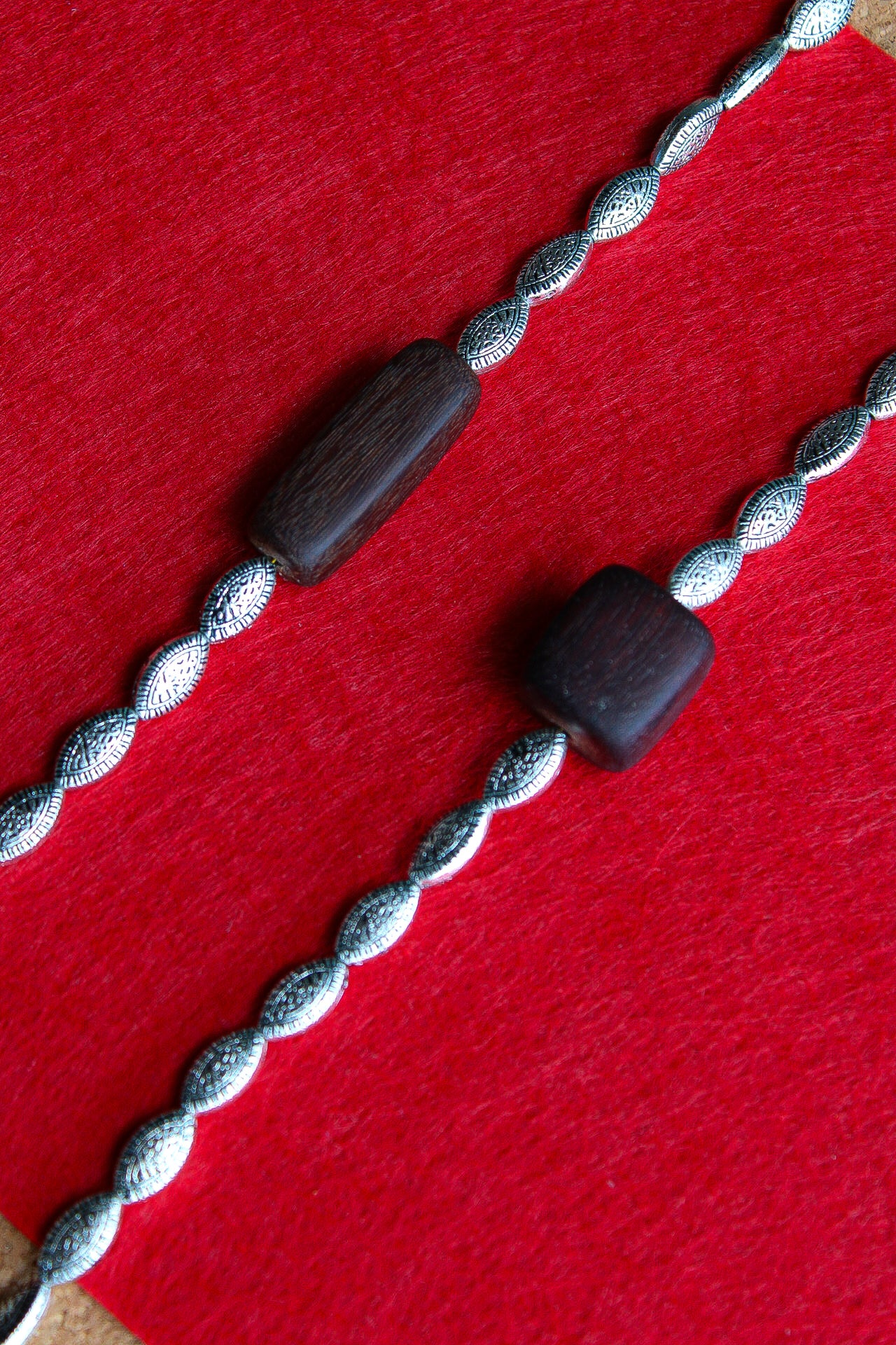 Two silver-toned twisted rope bracelets with dark brown wooden beads, laid diagonally on a textured red background.