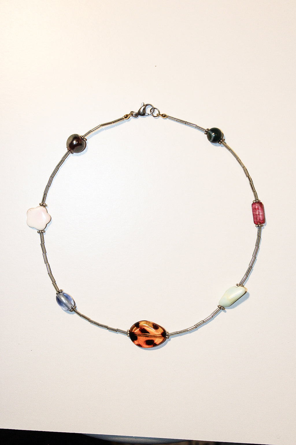 A handmade beaded necklace with a silver-toned wire chain and multiple decorative beads, including a prominent orange and black leopard print bead, on a plain off-white background.