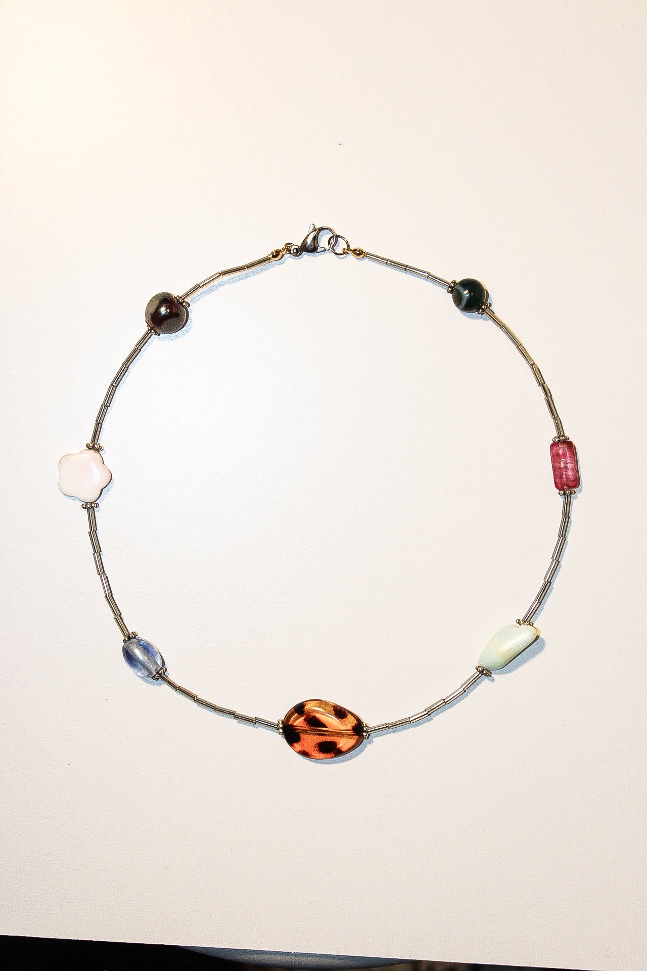 A handmade beaded necklace with a silver-toned wire chain and multiple decorative beads, including a prominent orange and black leopard print bead, on a plain off-white background.