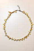 A handmade beaded necklace featuring irregular cream and yellow faux pearls, polished amber-like beads, and small metallic spacer beads on a silver-tone chain with an extender clasp, displayed on a plain off-white background.