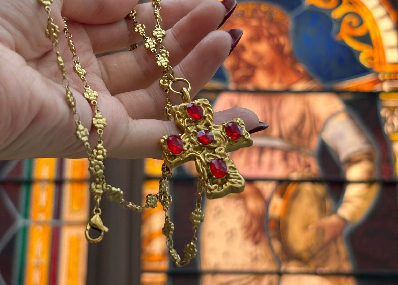 Gold necklace with red stones held in front of a stained glass window